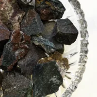 Rå blodsten krystal i skål med flere andre. grøn tyrkis og rødlige nuancer.